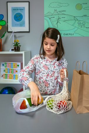 Student taking fruits from disposable plastic bag to reusable mesh bag in ecology classroom