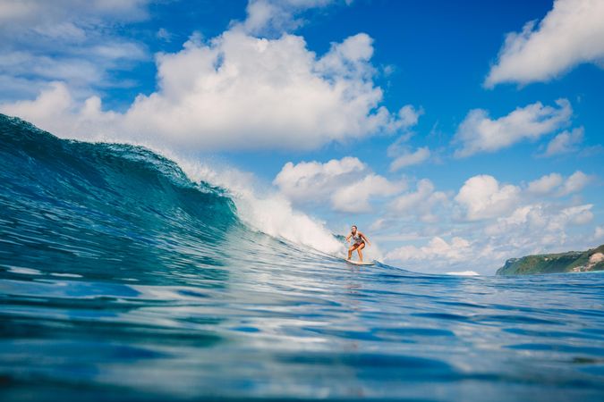 Woman surfing on sea waves under blue and sunny cloudy sky