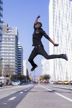 Black man wearing casual clothes jumping on street in city