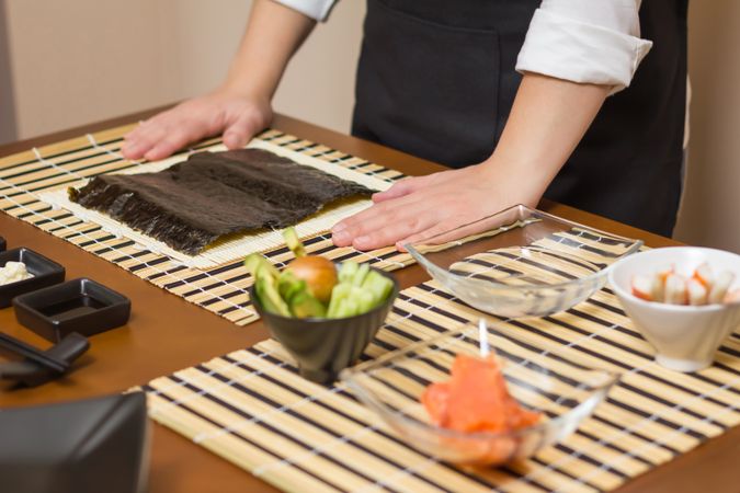 Hands of chef ready to prepare Japanese sushi rolls, with principal ingredients in the foreground