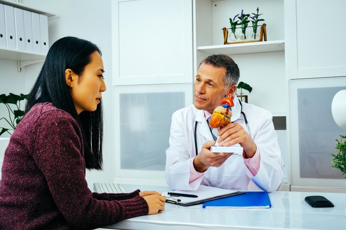 Male doctor with serious female patient consulting about heart structure