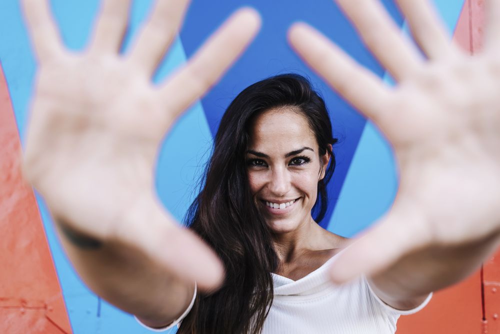 Smiling woman leaning against a wall while framing the face with hands