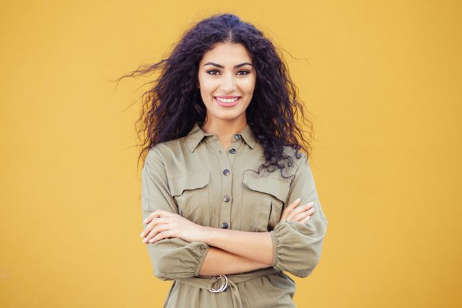 Female in army green jumpsuit smiling in front of mustard wall