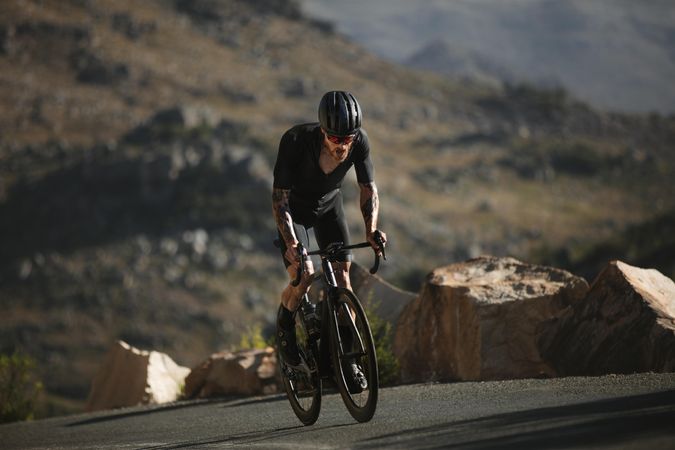 Strong biker charges up steep asphalt road on mountain