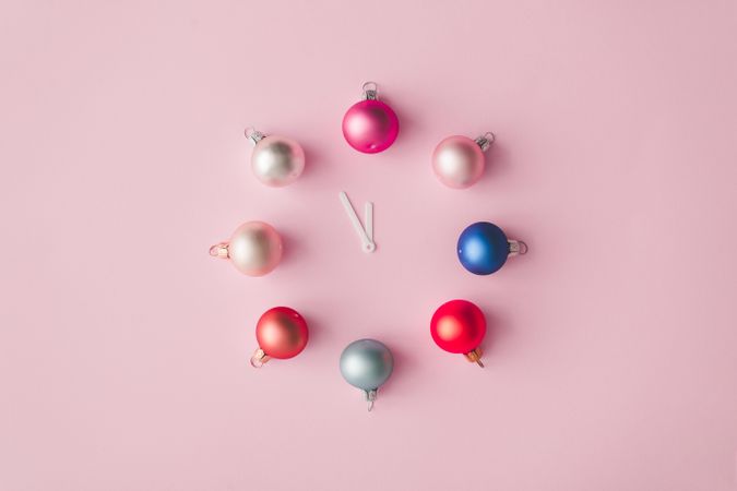 Clock hands with colorful pastel decoration balls on pink painted wall