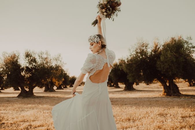 Content woman in dress with open back raising hands with flower bouquet