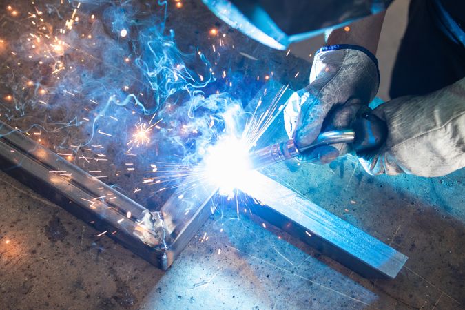 Welder in protective helmet welding metal detail in workshop