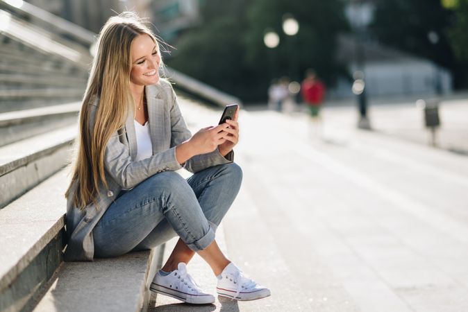 Smiling woman sitting on steps checking phone