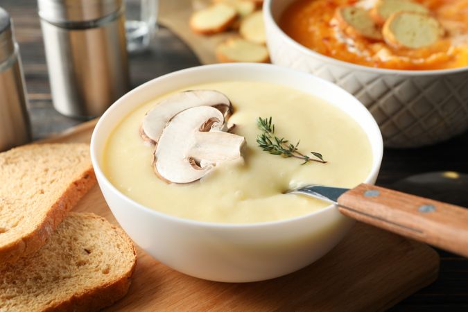 Bowl of mushroom soup next to pumpkin soup on table with bread