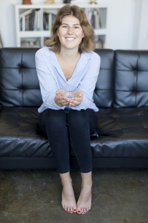 Female drinking water sitting on a couch at home and looking at camera