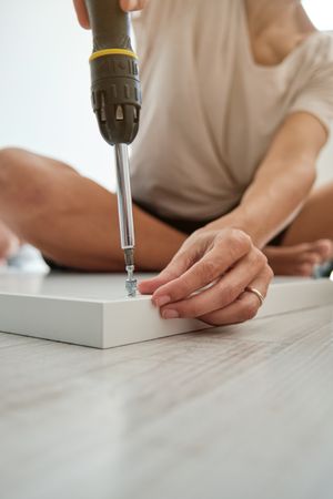 Unrecognizable woman screwing clincher into wooden plank