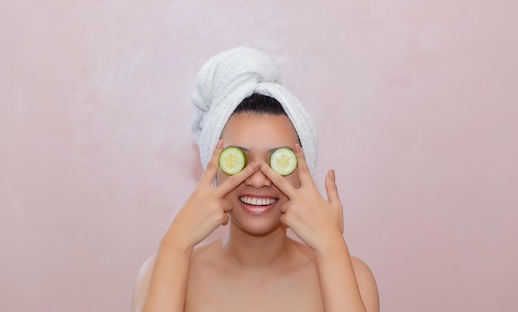 Young woman covering her eyes with cucumber