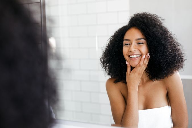Smiling Black woman with curly hair looking in the mirror touching her chin