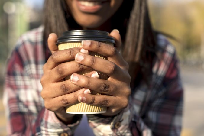 Close up of female’s hands in plaid shirt holding a to go coffee