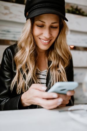 Smiling curly woman browsing smartphone at table