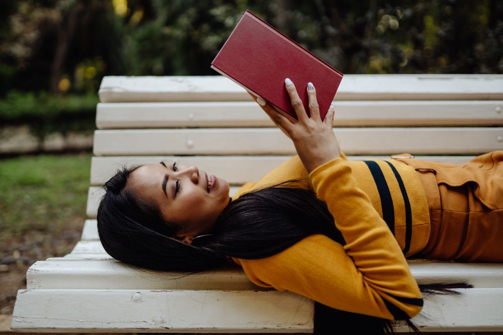 Graceful long haired Asian woman reading book on bench in park