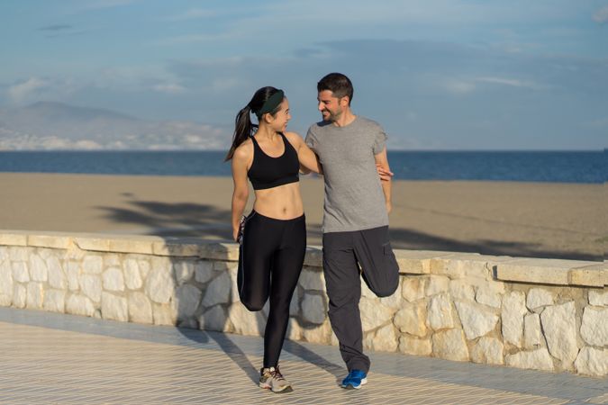 Young couple in active wear going stretching exercises together at seaside