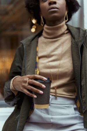 Close-up shot of Black woman in green jacket holding a cup of coffee