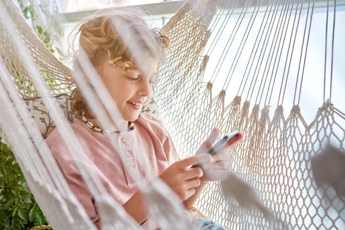 Cheerful boy using smartphone while resting in hammock