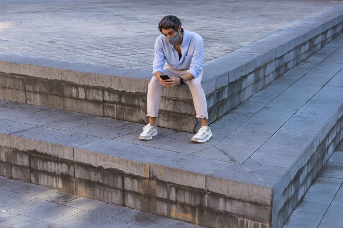 Man in mask browsing smartphone on street