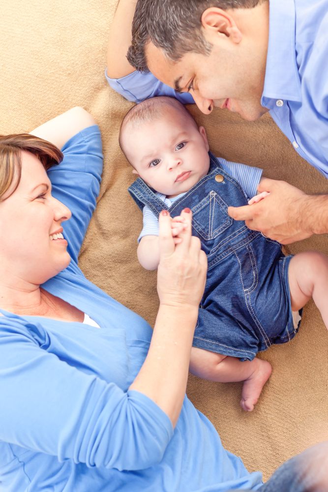 Young Couple Laying With Their Infant On A Blanket
