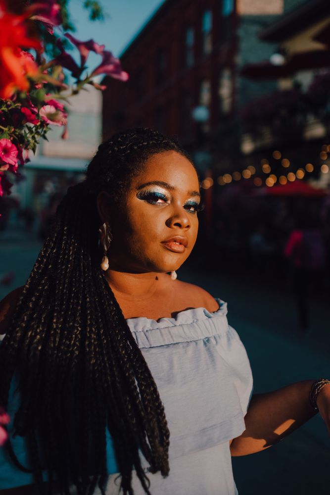 Joyful trendy Black woman standing beside blossomed tree