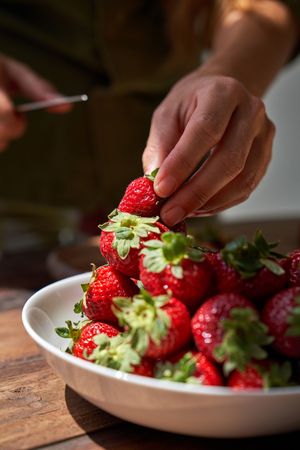 Crop person taking strawberry from bowl
