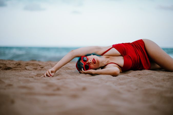 Relaxed woman in bright stylish swimsuit lying on sandy beach