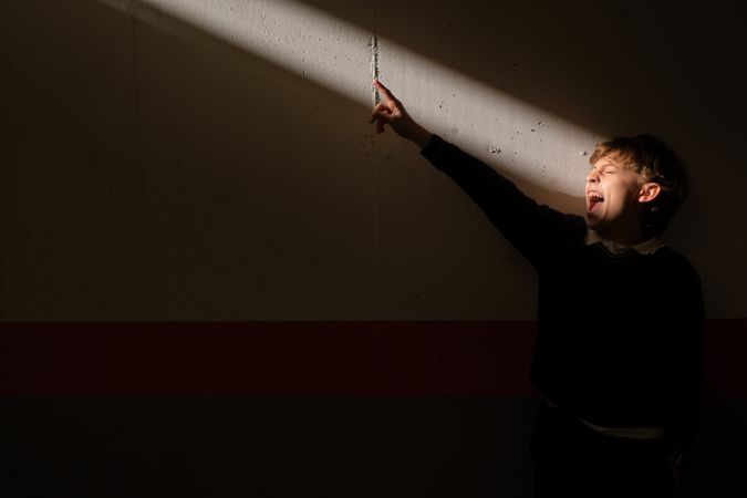 Preteen boy standing in sunbeam screaming and pointing finger