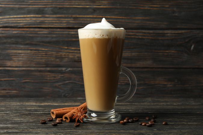 Glass cup of latte, coffee seeds and cinnamon on wooden background