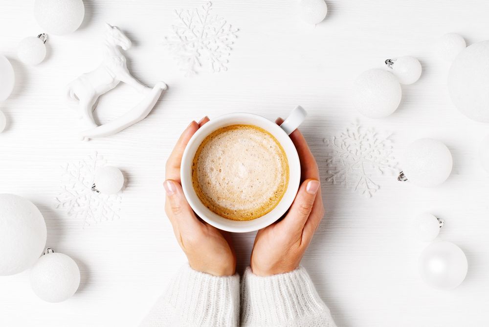 Hand holding a warm Christmas beverage surrounded by decorations