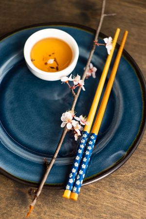 Table setting with chop sticks on ceramic navy plate and decorative cherry blossom branch and cup of tea