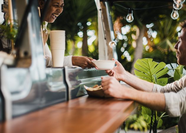 Woman serving food to customer inside food truck - Focus on hands holding food plate
