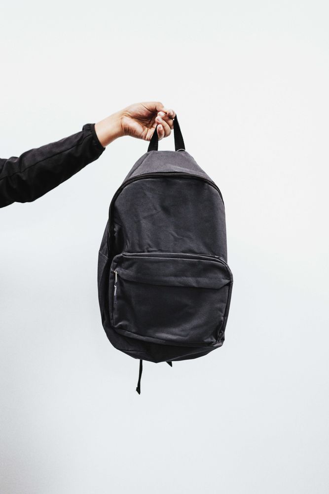 Cropped image of a hand holding a dark backpack against light background