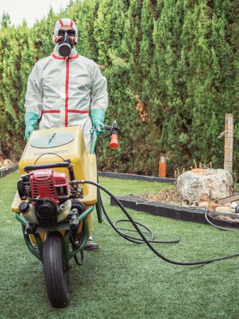 Specialist in uniform for fumigation holding yellow trolley in yard