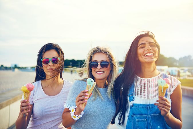 Three smiling female friends enjoying ice cream in the sun