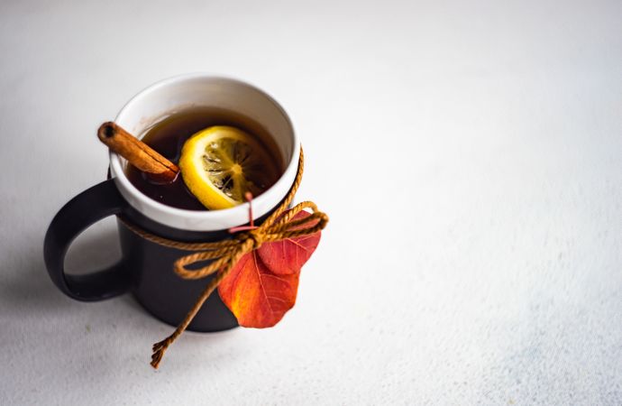 Mug of warming tea with cinnamon stick and lemon slice decorated with fall leaf