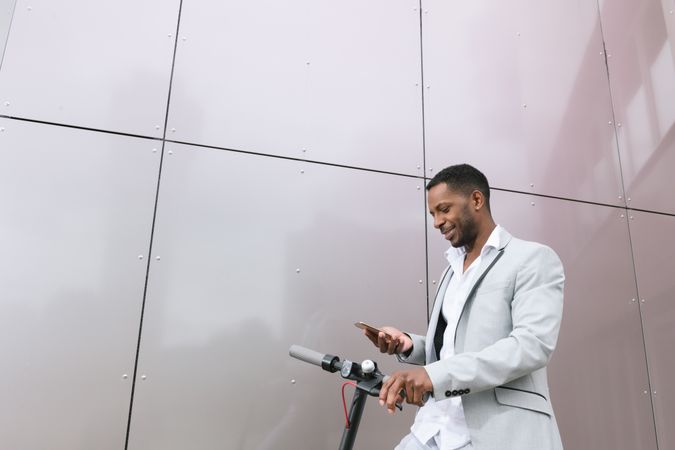 Smiling Black man riding scooter and speaking on smartphone