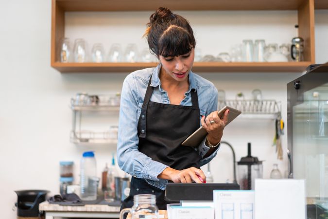 Woman in apron working in cafe with digital tablet in hand