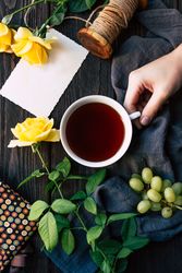 Crop hand with tea near flowers and blank note