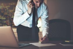 Professional man speaking on his phone while writing on documents