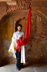Man in traditional outfit holding red fabric indoor