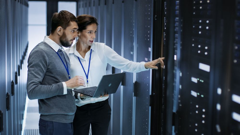 Male IT Specialist Holds Laptop and Discusses Work with Female Server Technician.