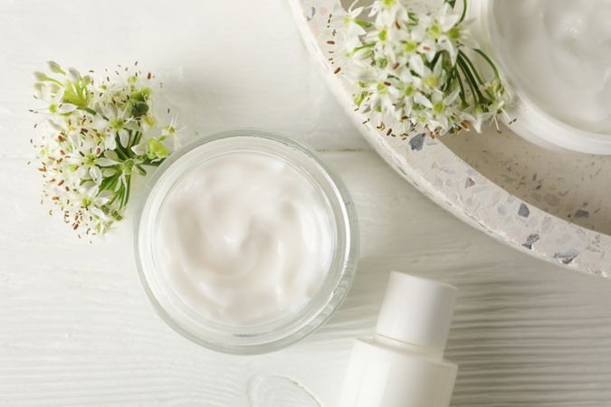 Cosmetic cream, tray and allium flowers on wooden background, top view