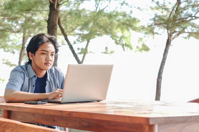 Serious Asian Young businessman work at outdoor with laptop. Concept of remote and freelance work. Young successful man wearing casual blue cloth.