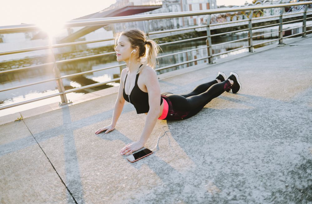 Woman with earphones and smartphone stretching on embankment
