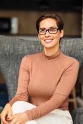 Portrait of smiling woman with short hair and eyeglasses sitting in turtleneck