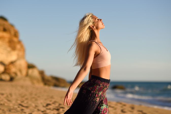 Woman stretching her arms facing the ocean on beach at sunset