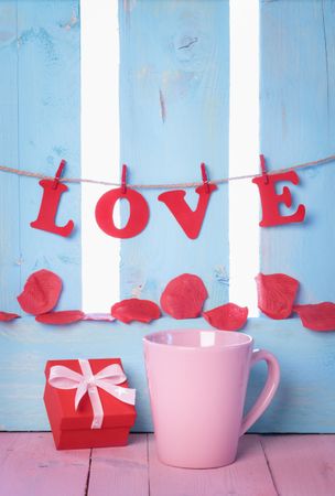 Red gift, pink coffee cup and the word love spelled out hanging on a banner