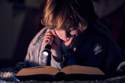 Focused boy reading book with flashlight